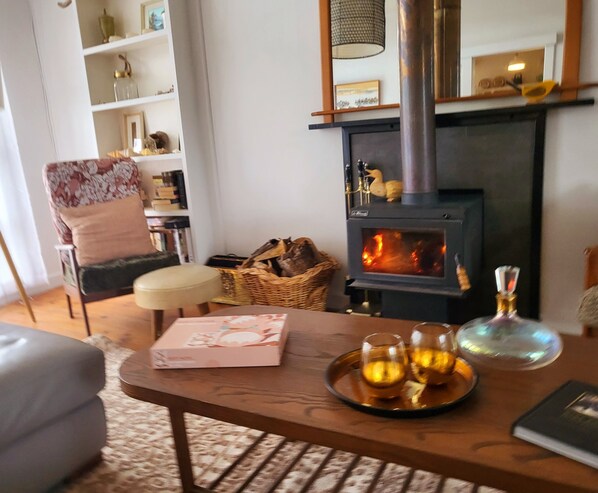 Un salon chaleureux avec une cheminée, un fauteuil confortable, une petite table avec des boissons et une bibliothèque.