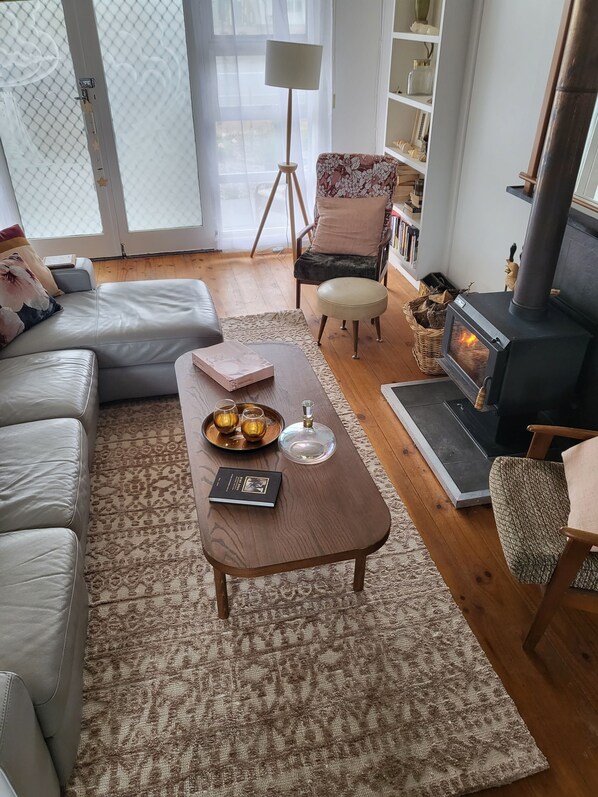 Ein gemütliches Wohnzimmer mit einer Couch, einem Couchtisch mit Getränken und einem Buch, einem Kamin und einem Bücherregal.
