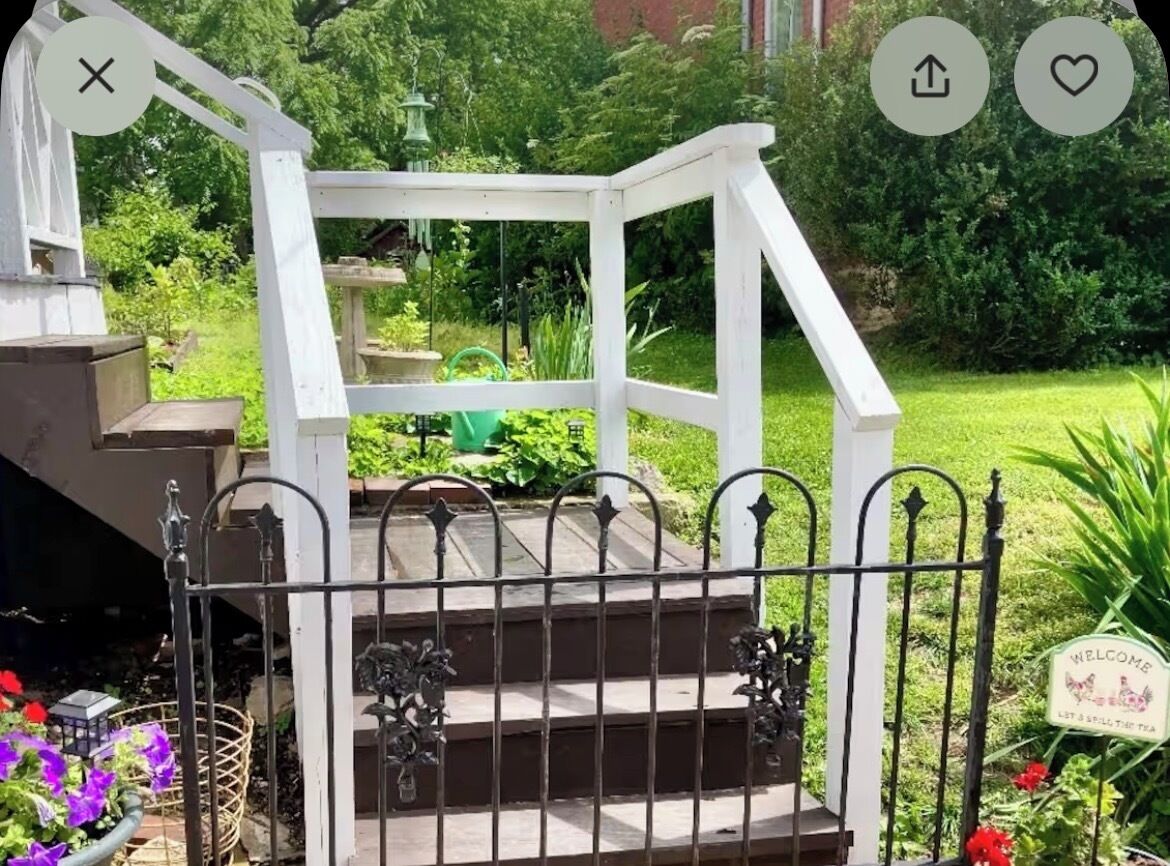 A white wooden staircase with a metal railing leading to a garden area.