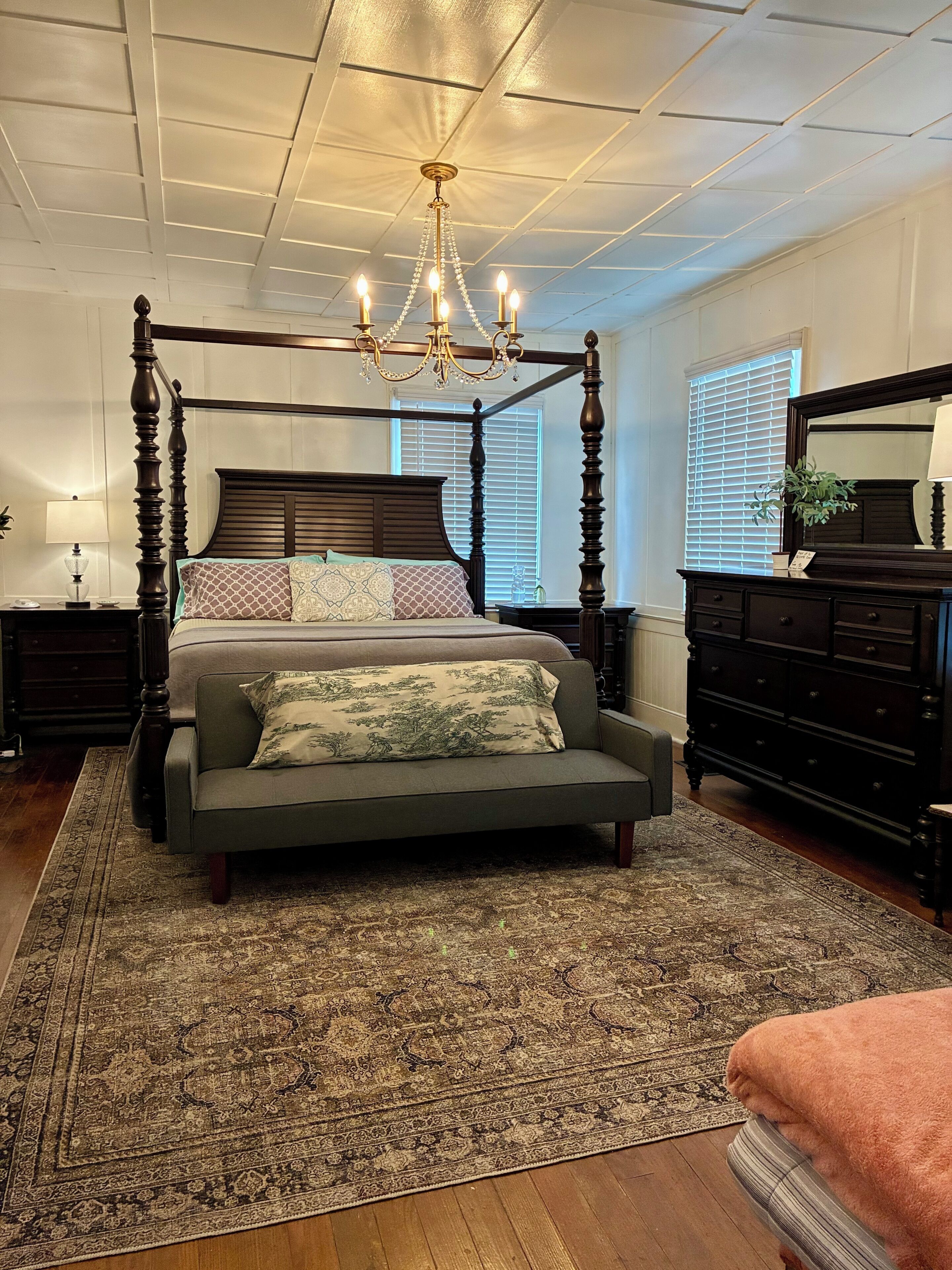 A four-poster bed with a chandelier, a large mirror, and a dark wooden dresser.