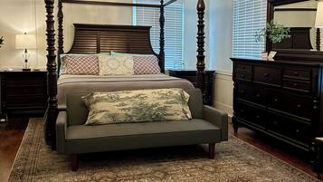 A four-poster bed with a chandelier, a large mirror, and a dark wooden dresser.