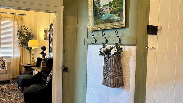 A room with a green wall, a painting, a wicker basket, and a patterned bench.