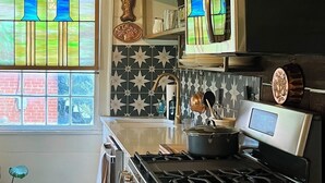 A kitchen with a black stove, stainless steel appliances, a patterned backsplash, and a window with stained glass.