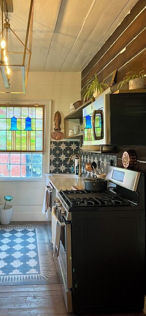 Et køkken med sort komfur, rustfrie hvidevarer, et mønstret backsplash og et vindue med farvet glas.