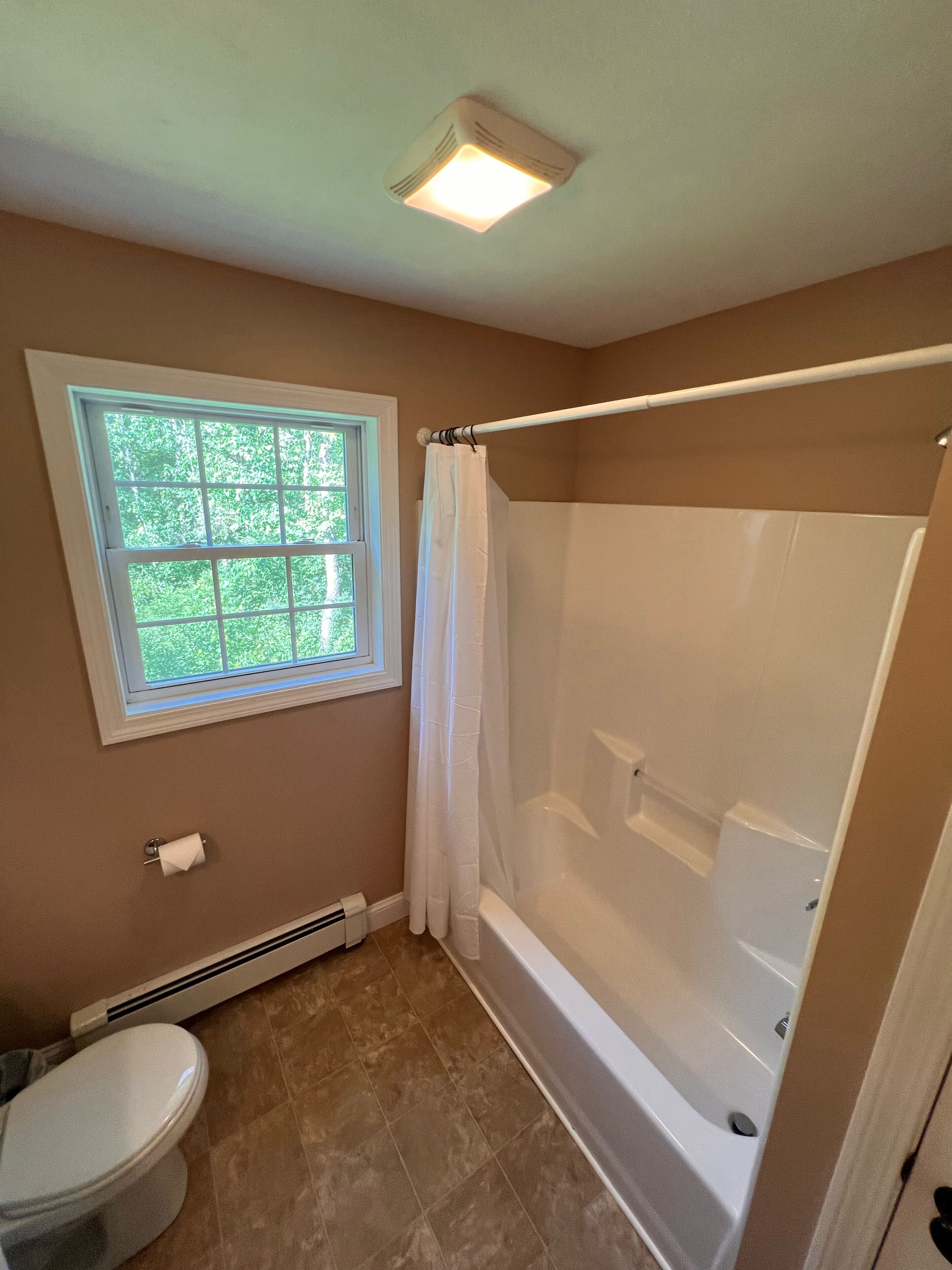 A bathroom with a window, a toilet, a shower, and a bathtub.
