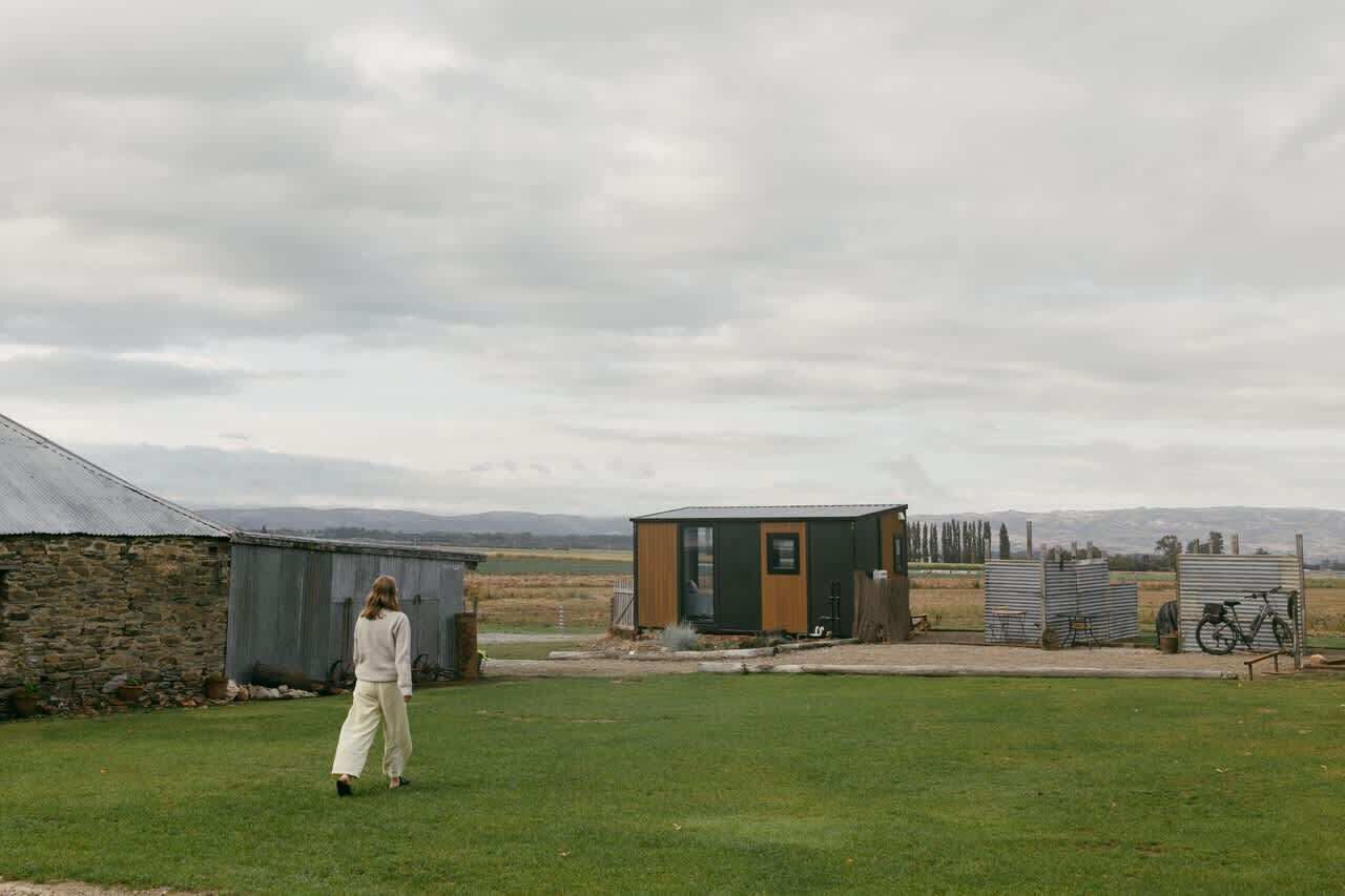A rural setting with a small wooden structure, a stone building, and a grassy field.