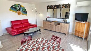 Una sala de estar con un sofá rojo, una mesa de centro de vidrio, un tapete estampado, un mueble de madera y un televisor sobre un soporte.