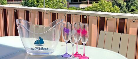 A table with a clear pitcher and three wine glasses on a balcony with a view of buildings and trees.