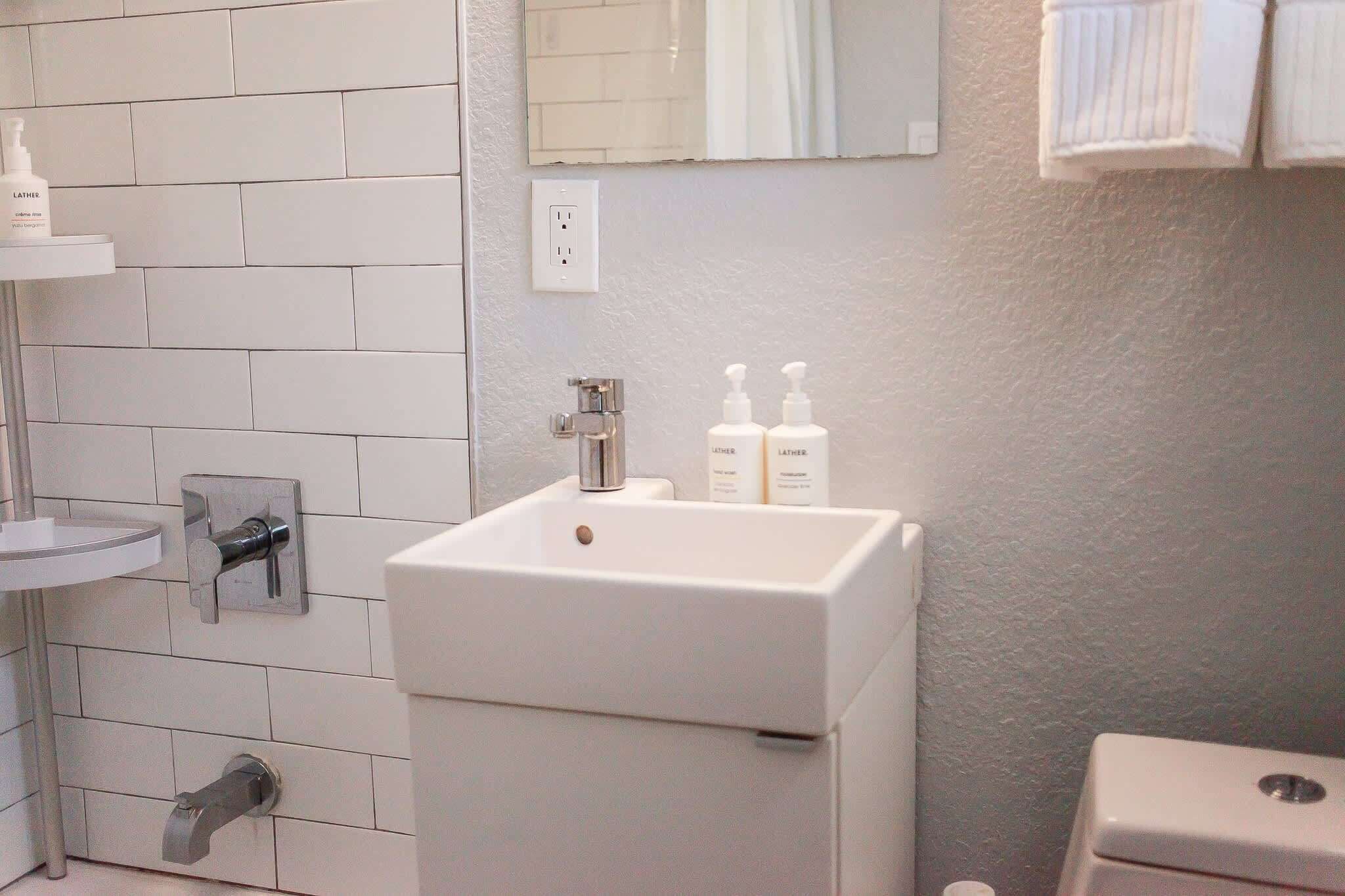 Un baño con un lavamanos blanco, un espejo y dos botellas de loción sobre el lavamanos.