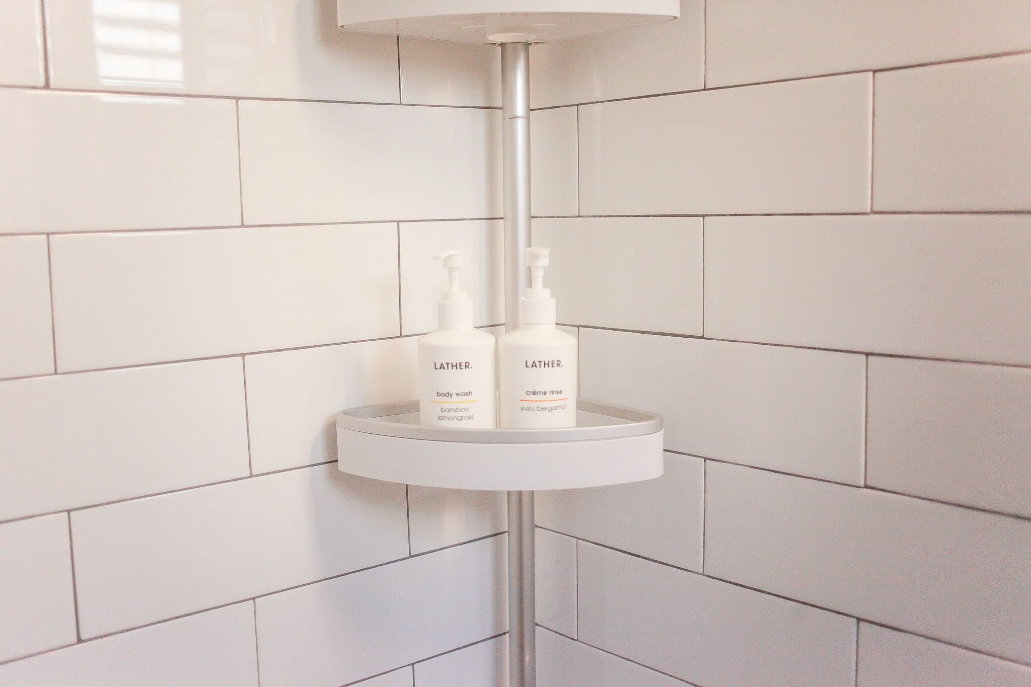 Un baño con azulejos blancos, un lavamanos blanco y dos botellas de jabón líquido Lather sobre el lavamanos.