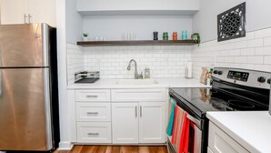 Una cocina moderna con armarios blancos, un refrigerador de acero inoxidable, una estufa negra y una encimera blanca.