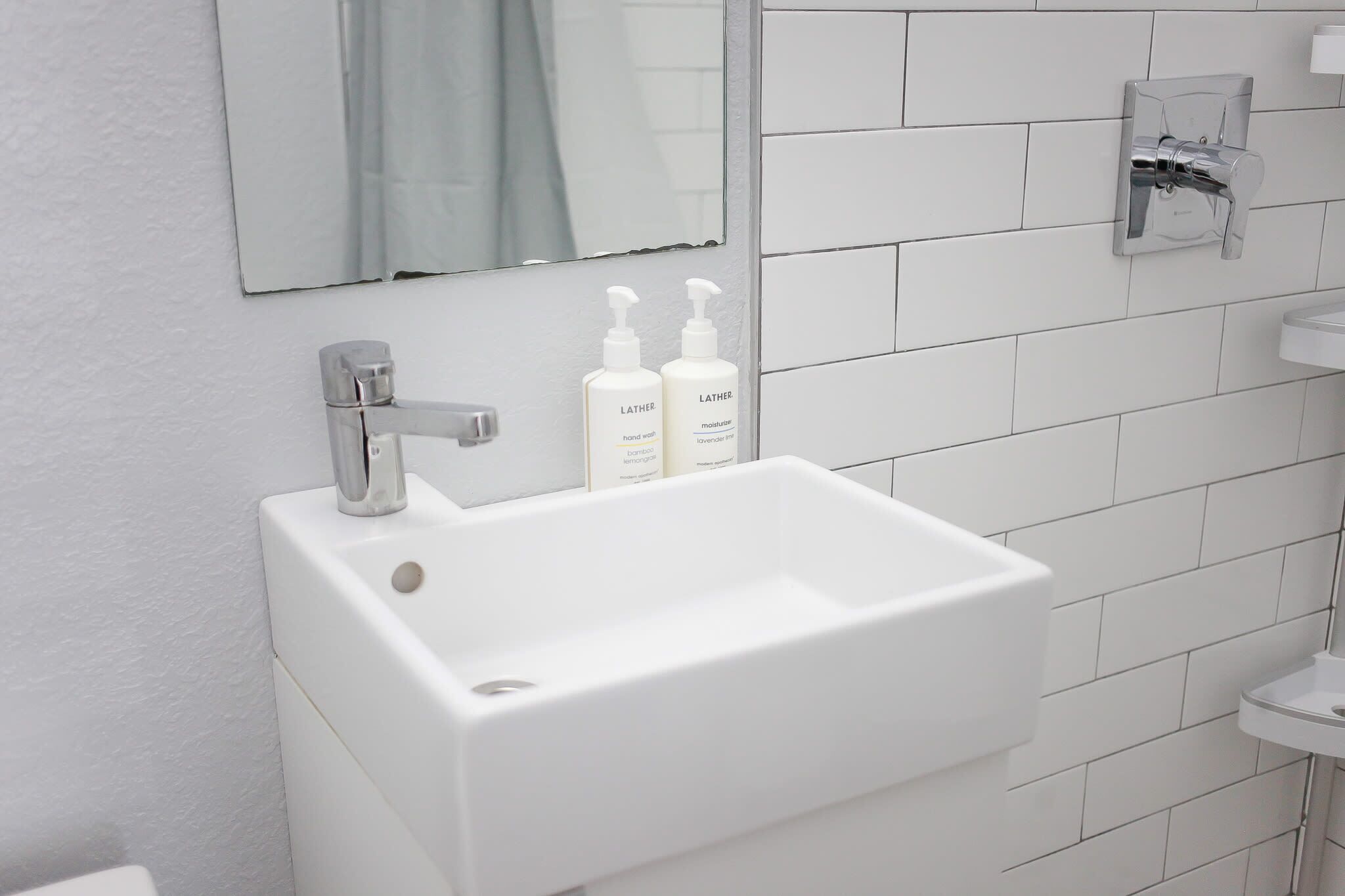 Un baño con lavamanos blanco, un espejo y dos botellas de jabón para manos.