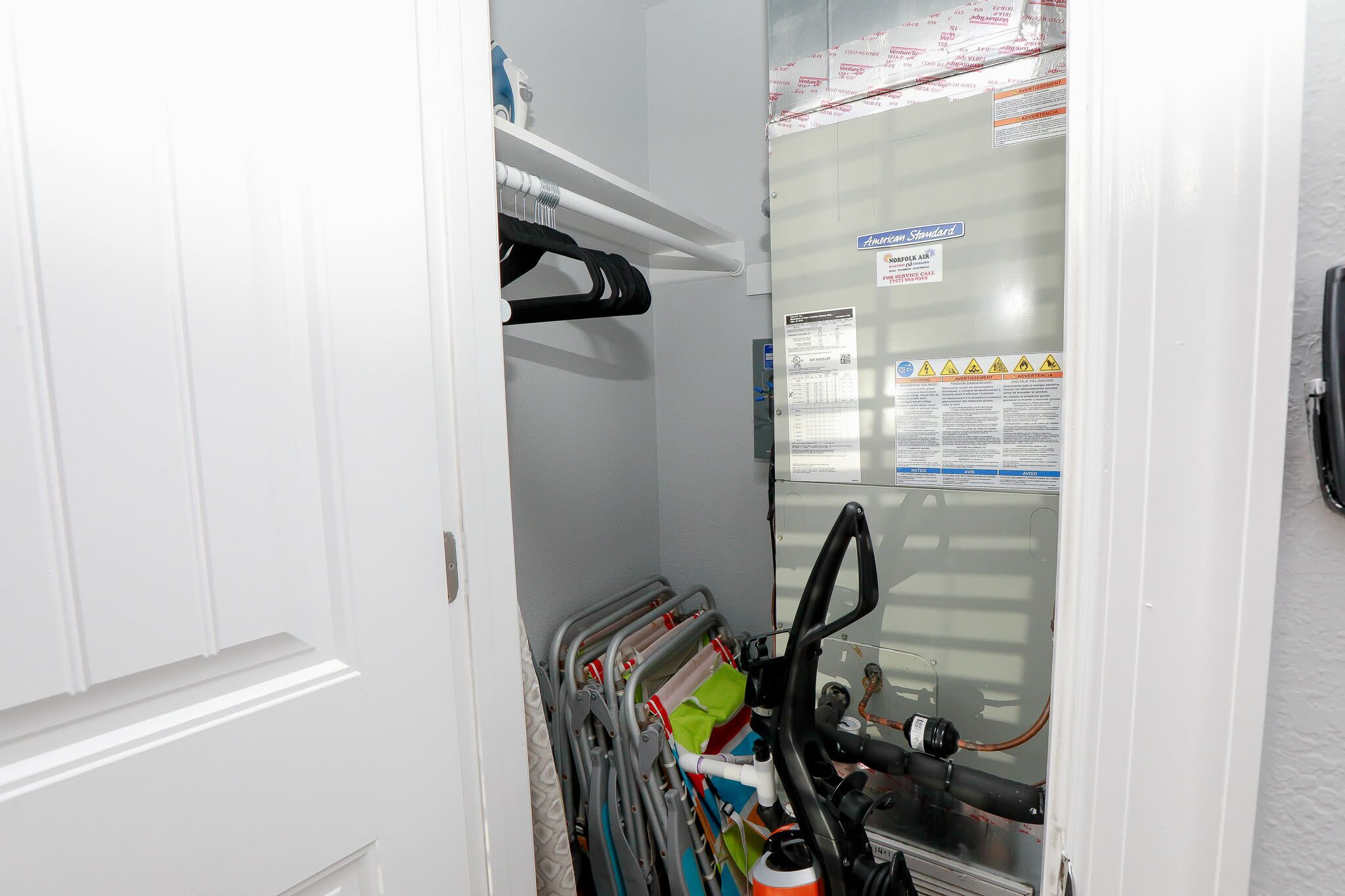 Une pièce utilitaire où l’on peut voir des panneaux électriques, des tuyaux et une étagère métallique sur laquelle sont rangés divers objets.