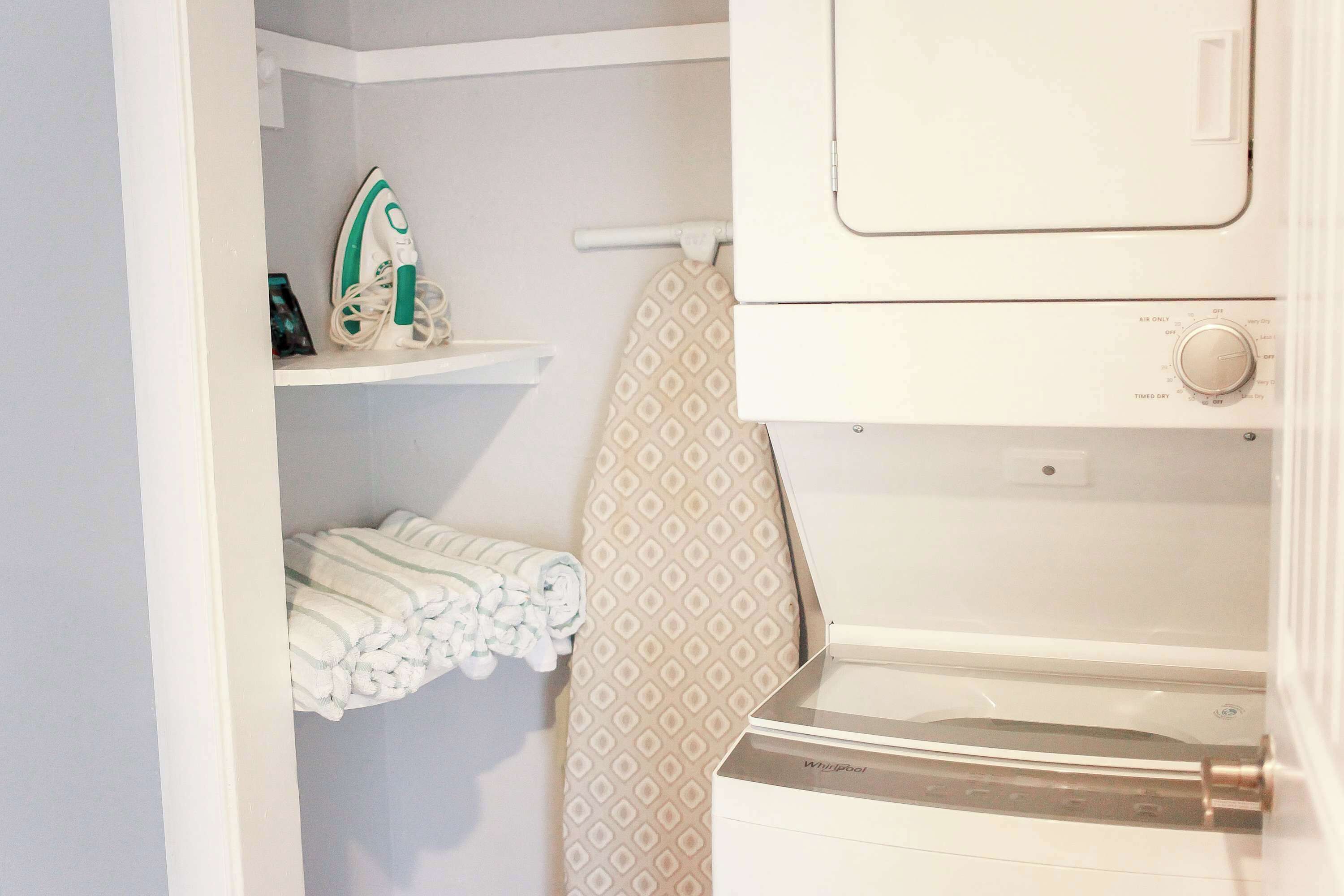 A laundry area with a washing machine, an iron, and neatly folded towels on a shelf.