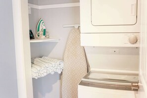 Un espace dédié à la lessive, comprenant un lave-linge, un fer à repasser et des serviettes soigneusement pliées, rangées sur une étagère.