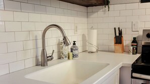 A kitchen with white tiled backsplash, stainless steel sink, and modern appliances. - Sojourn Palm Suite at Beach Cottages (Norfolk)