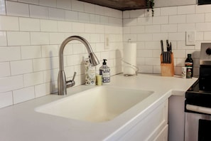 Una cocina con salpicadero de azulejos blancos, pileta de acero inoxidable y electrodomésticos modernos.