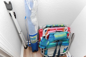 Un rincón de una habitación con pared, puerta y suelo blancos. Hay un poste blanco con un accesorio negro en la pared, una mosquitera azul y blanca y un cochecito con tela de colores y un bolso azul.