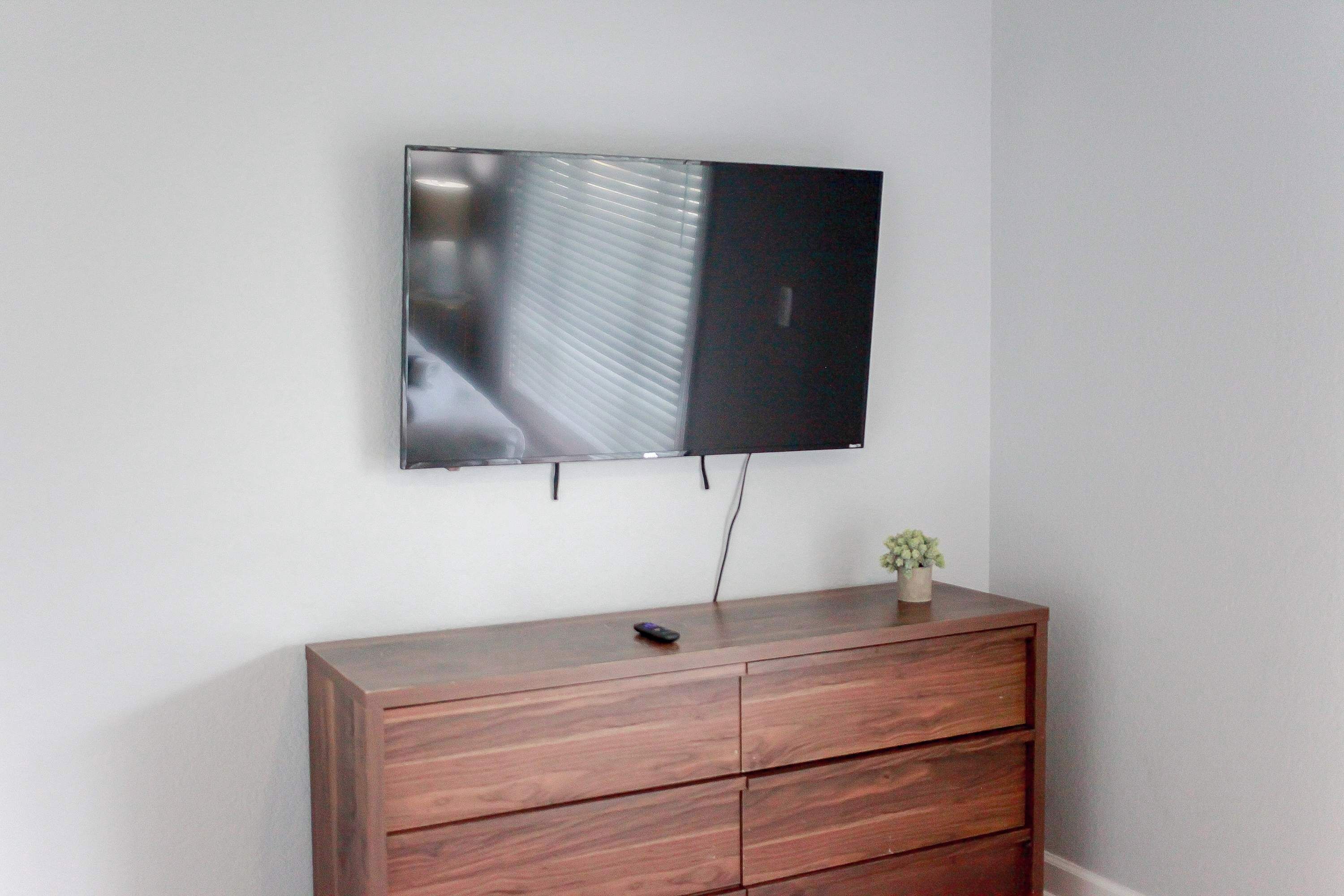 Ein Flachbildfernseher ist an einer Wand über einer Holzkommode mit Schubladen angebracht.