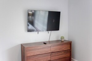 A flat-screen TV mounted on a wall above a wooden dresser with drawers. - Sojourn Palm Suite at Beach Cottages (Norfolk)