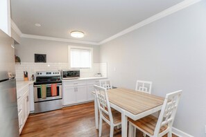 A modern kitchen with white cabinets, a wooden dining table, and a built-in oven. - Sojourn Palm Suite at Beach Cottages (Norfolk)