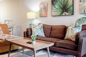 Un salon avec un canapé en cuir marron, une table basse en bois et une lampe. Deux tableaux sont accrochés au mur, et une plante en pot est posée sur la table basse.