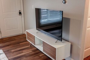 Un salon moderne avec un téléviseur à écran plat posé sur un meuble TV blanc, un plancher en bois et une porte blanche.