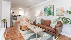 A modern living room with a brown leather sofa, a wooden coffee table, and a patterned rug. - Sojourn Palm Suite at Beach Cottages (Norfolk)