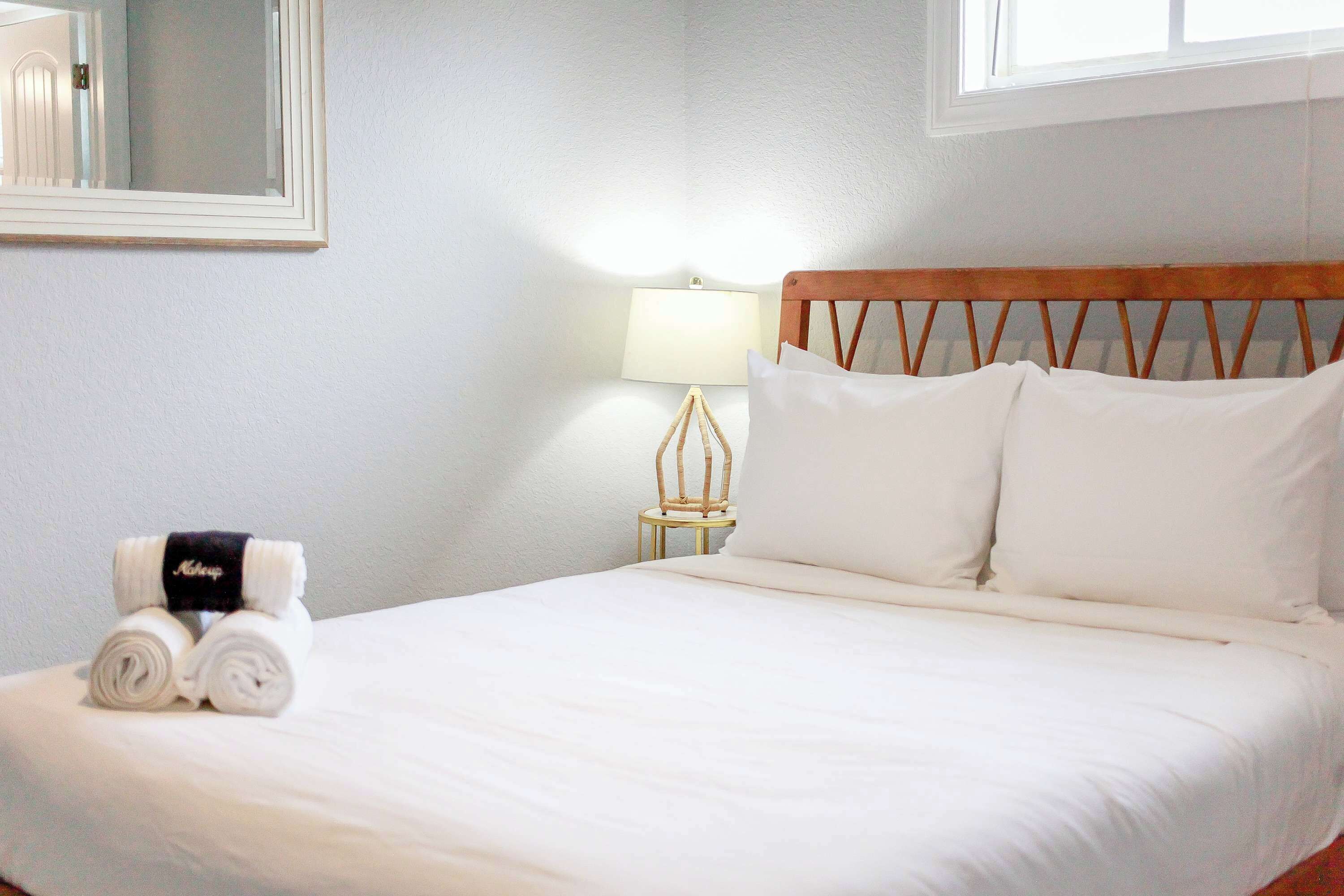 A neatly made bed with white linens, a wooden headboard, and a small bedside table with a lamp.