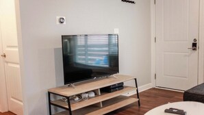 A living room with a flat-screen TV on a wooden stand, a white coffee table, and a door in the background. - Sojourn Beach Suite 2 BR 2 BA at Beach Cottages (Norfolk)