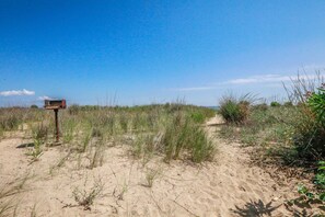 Un sendero arenoso que atraviesa una zona cubierta de hierba, con un cartel indicador a la vista.