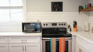 A kitchen with white cabinets, a microwave, an oven with a colorful towel, and a stove. - Sojourn Beach Suite 2 BR 2 BA at Beach Cottages (Norfolk)