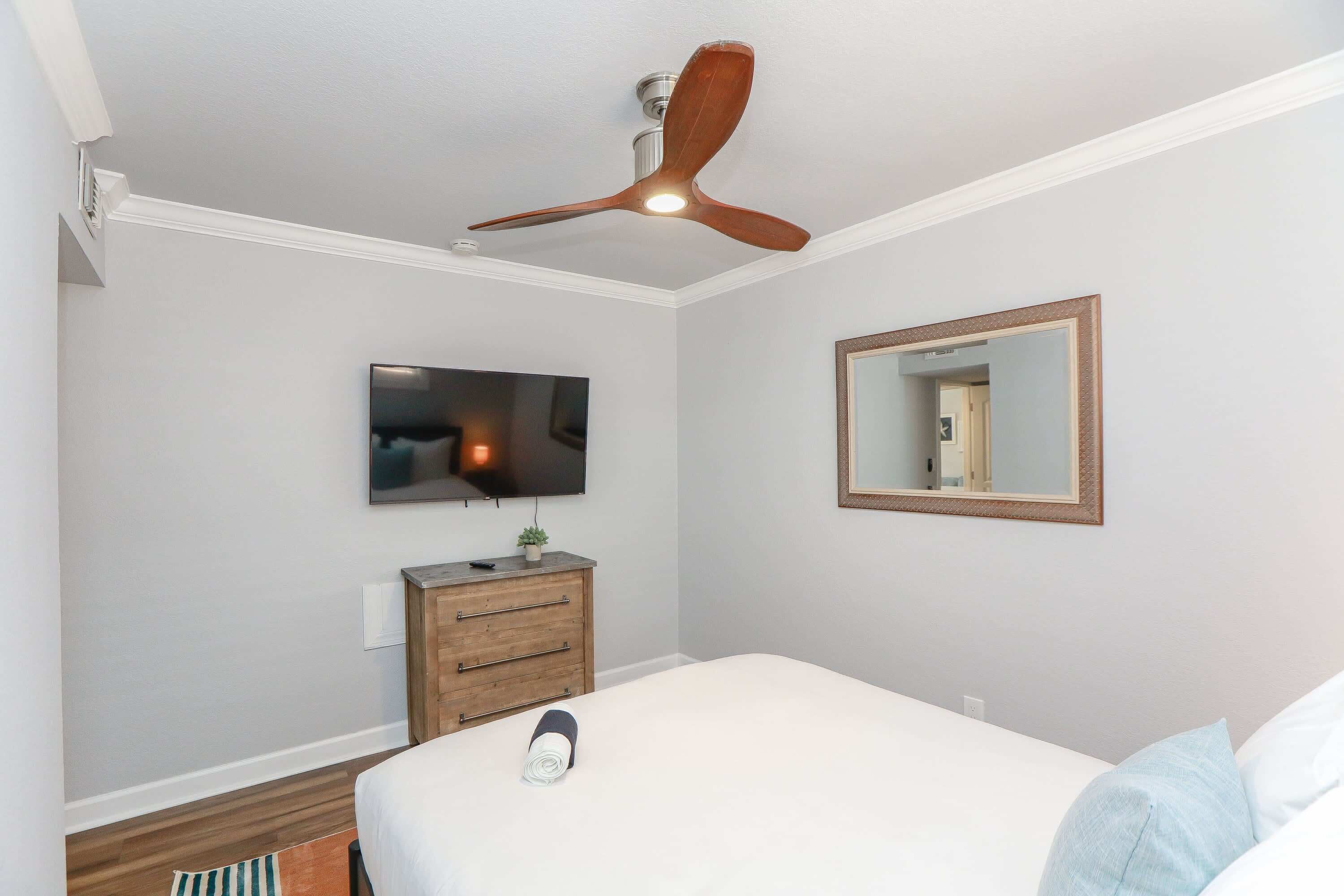 A bedroom with a bed, a ceiling fan, a television, a dresser, and a mirror.