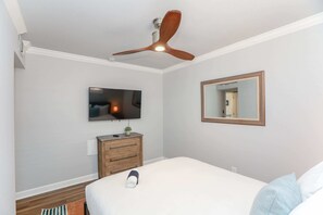 A bedroom with a bed, a ceiling fan, a television, a dresser, and a mirror.