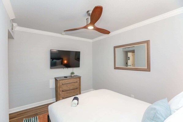 A bedroom with a bed, a ceiling fan, a television, a dresser, and a mirror.