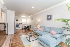 A modern living room with a blue sofa, a glass coffee table, and a dining area with a white table and chairs.