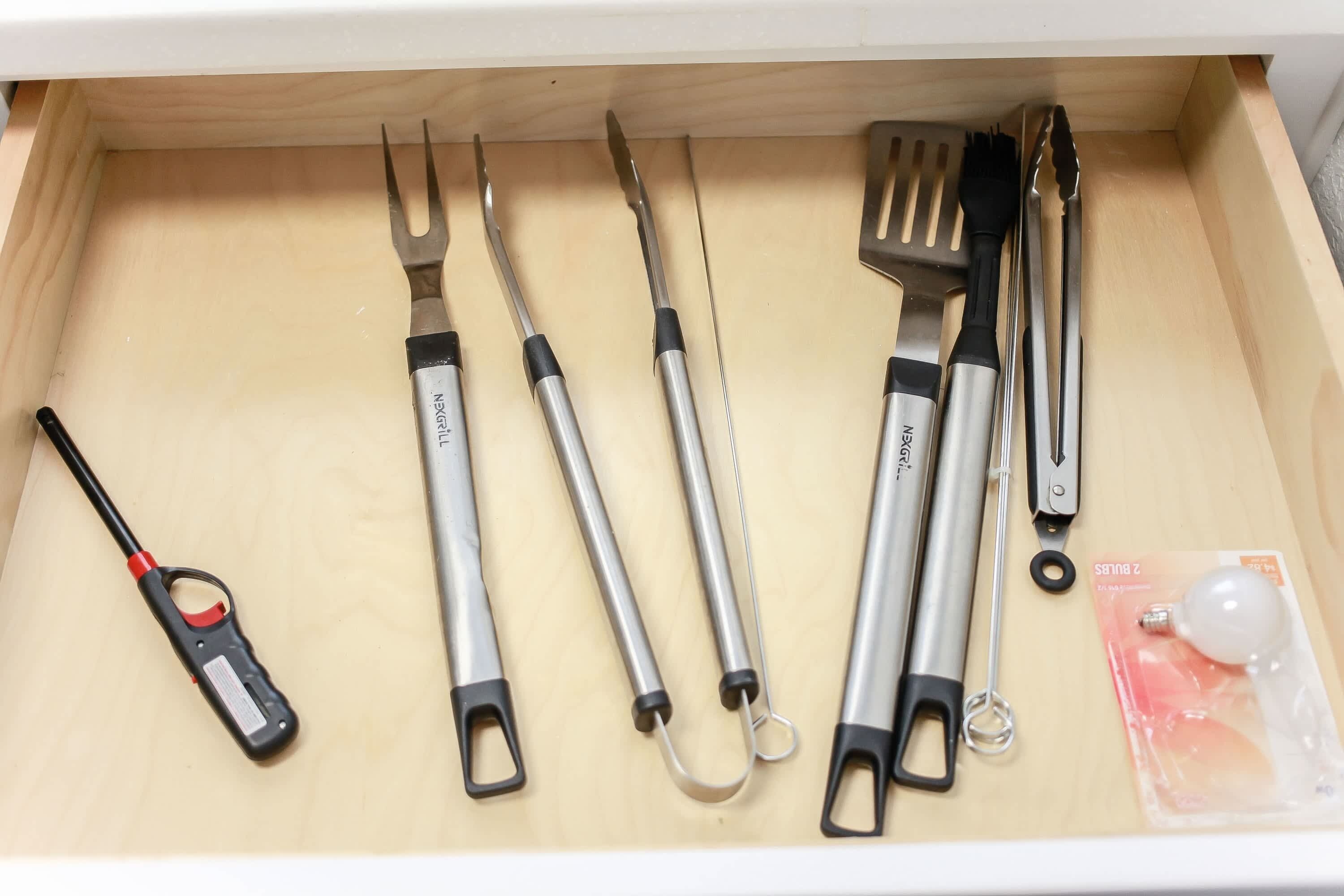 Un tiroir contenant divers ustensiles de cuisine, notamment une pince, une spatule et un ouvre-boîte.