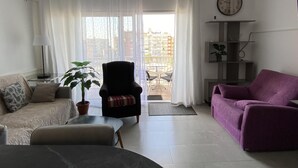 Un salon avec un canapé, un fauteuil et un fauteuil violet. On y trouve également une plante en pot, une lampe et une horloge au mur.