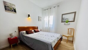 Une chambre bien rangée, avec un lit en bois, une table de chevet avec une lampe, une chaise et un miroir fixé au mur.