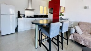 Une cuisine moderne dotée d’un îlot central, de meubles blancs, d’un mur d’accent rouge et d’un coin repas avec des tabourets de bar.