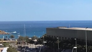 Une vue sur la côte, avec un bâtiment, une zone de stationnement et des bateaux au loin.