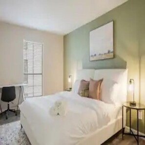 Relax in a cozy space with a comfortable bed, desk, and window with blinds.