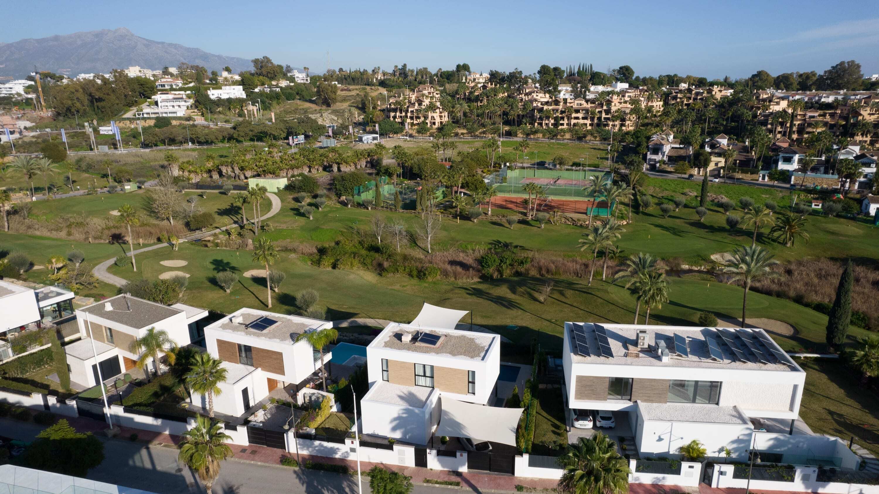Quartiere residenziale con case moderne, un campo da golf e una montagna sullo sfondo.