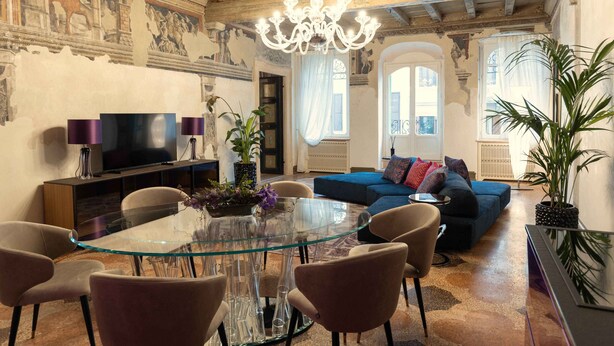 A spacious living room with a glass-top dining table, comfortable seating, a large sofa, and a television. - MARIA CALLAS LUXURY APPARTAMENT (VERONA)