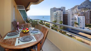 A balcony with a table set for two, overlooking a coastal cityscape with buildings and a mountain in the background. - Turmalina by Interhome (Calpe/Calp)