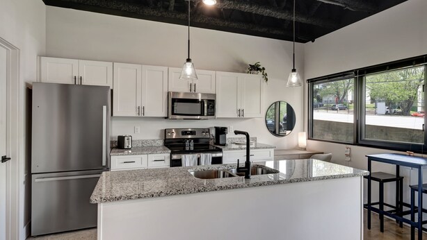 Una cocina moderna con armarios blancos, electrodomésticos de acero inoxidable, encimeras de granito e iluminación colgante.