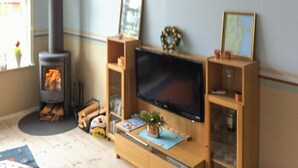 A living room with a fireplace, a flat-screen TV on a wooden stand, and shelves with various items. - 4 bedroom lovely home in Njurunda (Njurunda)