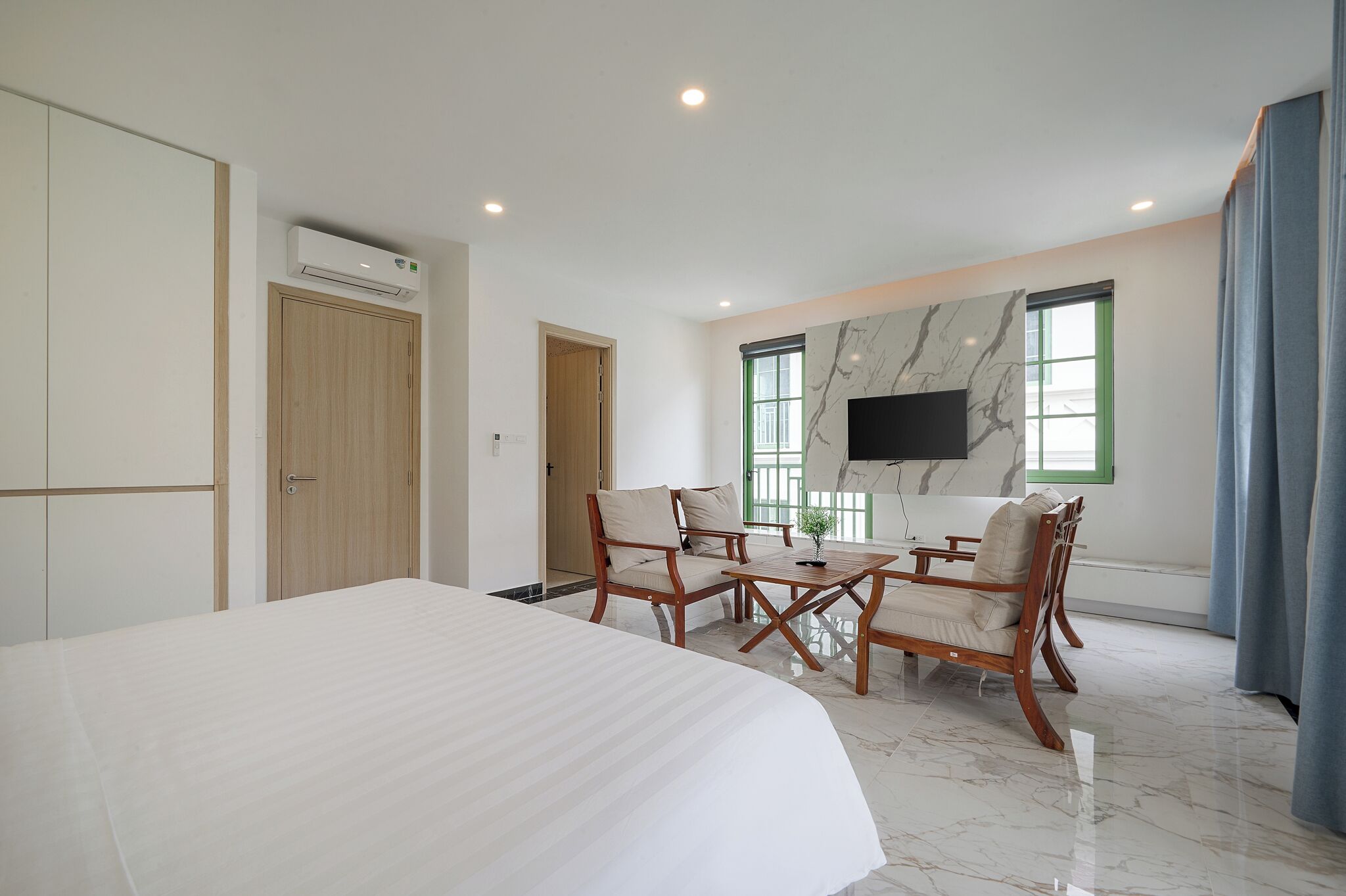 A hotel room with a large bed, wooden furniture, a flat-screen TV mounted on the wall, and a marble floor.