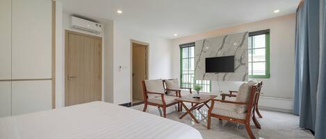 A hotel room with a large bed, wooden furniture, a flat-screen TV mounted on the wall, and a marble floor.