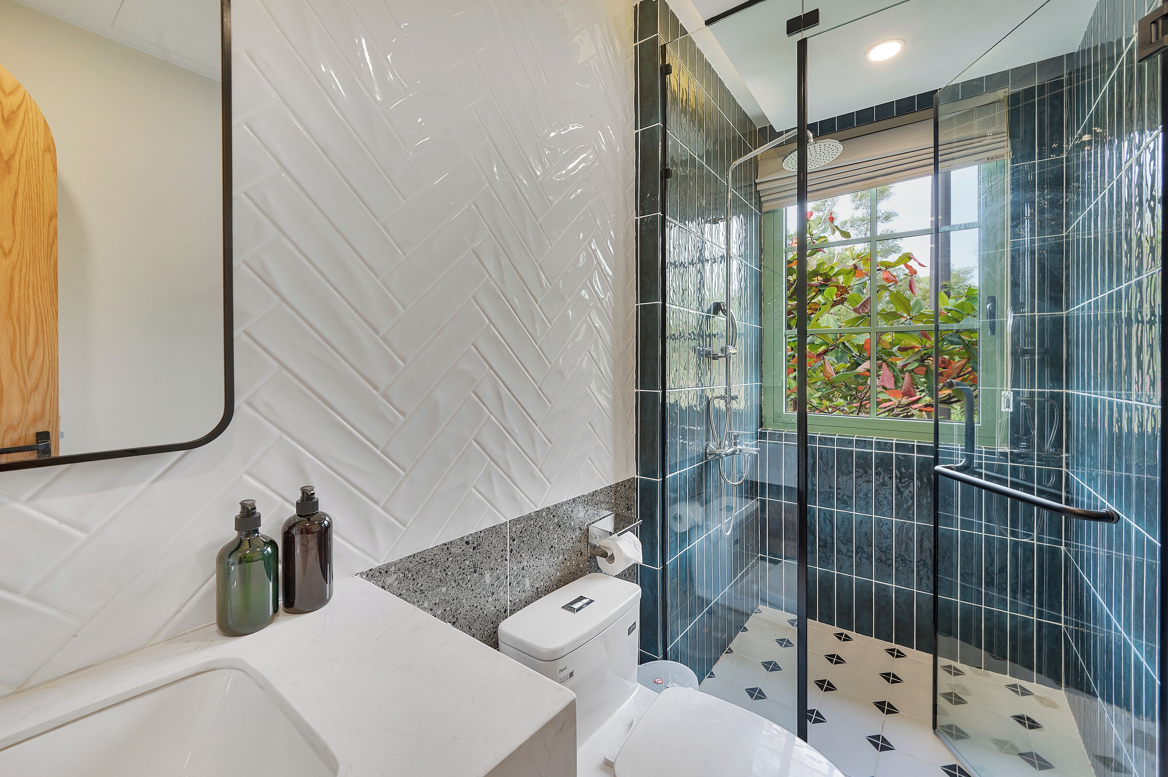 A modern bathroom with a glass-enclosed shower, white tiles, and a visible toilet paper holder.